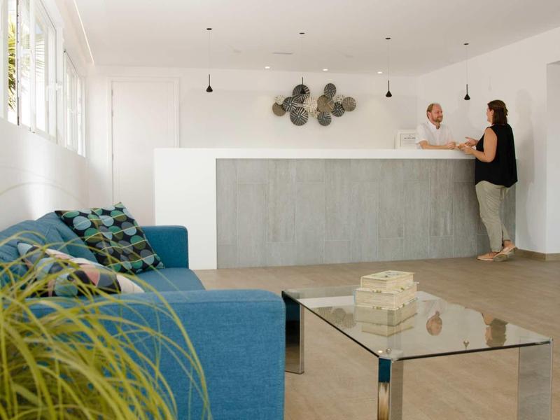 Moderner Wartebereich mit blauem Sofa, Glas-Couchtisch und einer sitzenden Frau am Empfangstresen.