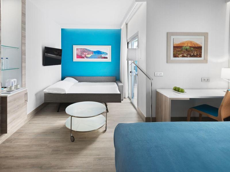 Camera d'hotel moderna con letto matrimoniale e singolo, accento blu e scrivania.