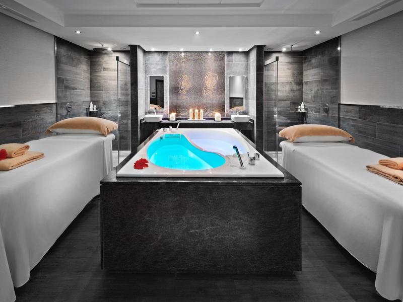 Locale spa di lusso con vasca idromassaggio tra due lettini da massaggio in ambiente scuro.