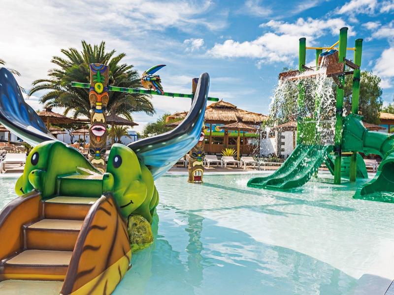 Area giochi acquatica per bambini con scivoli colorati in piscina sotto il sole.