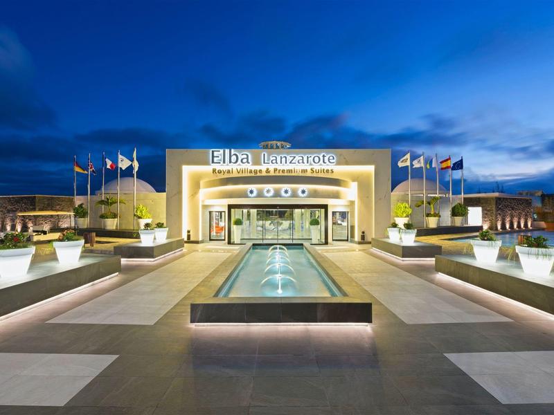 Ingresso di un hotel di notte con specchio d'acqua illuminato e bandiere.