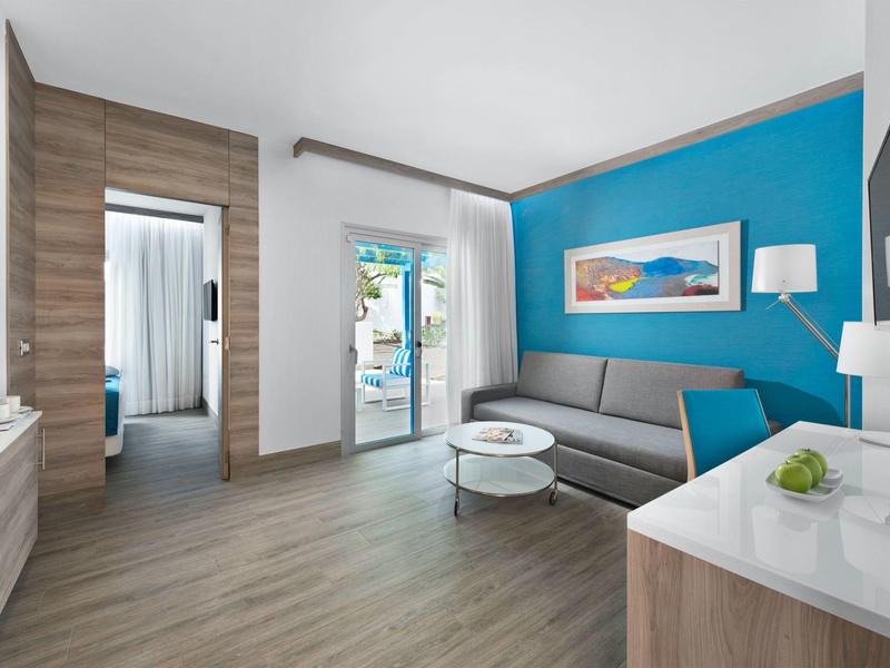 Camera d'hotel moderna con area salotto, pavimento in legno e parete con accento blu.