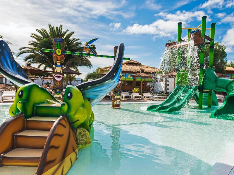 Scivolo d'acqua colorato con motivo di rana in una piscina dell'hotel sotto un cielo azzurro.