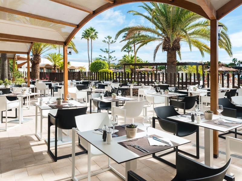 Ristorante con terrazza all'aperto con sedie nere e bianche sotto le palme al sole.