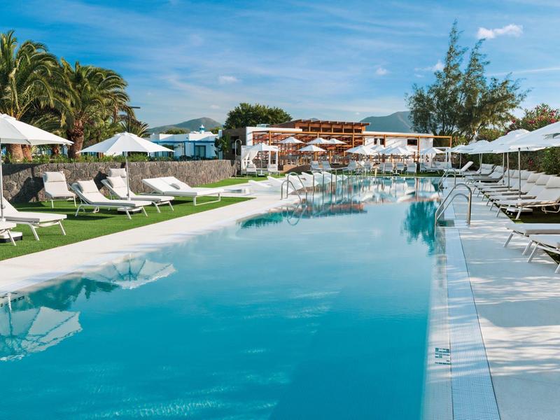 Lunga piscina con lettini bianchi e ombrelloni in un resort sotto il sole.