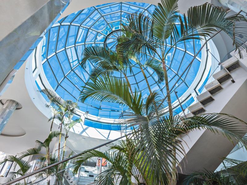 Interno di un atrio con una grande cupola di vetro e piante tropicali sotto.