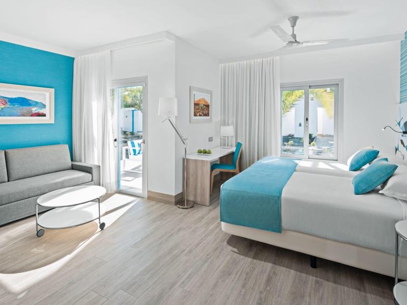 Camera d'hotel luminosa con letto matrimoniale, angolo salotto, scrivania e aria condizionata.