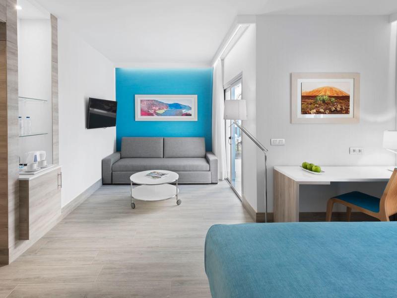 Camera d'hotel luminosa con divano moderno, opere d'arte murali e area scrivania.