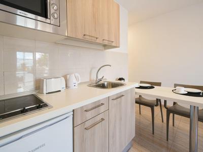 Moderne helle Küche mit Holzschränken, Herd, Spüle und kleinem Esstisch mit zwei Stühlen.