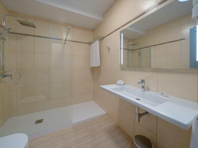 Modernes Badezimmer mit großer Regendusche, Doppelwaschbecken und hellen Wandfliesen.