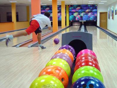 Ein Mann wirft eine Bowlingkugel in einer hell beleuchteten Bowlingbahn mit bunten Kugeln im Vordergrund.