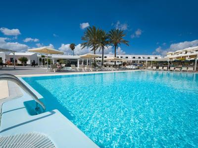 Großer Außenpool mit klar blauem Wasser vor Hotelgebäuden und Palmen unter blauem Himmel.