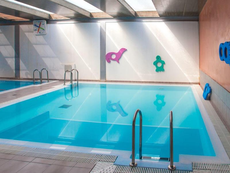 Innenhallen-Schwimmbad mit klar blauem Wasser, Treppen, weißen Wänden und bunten Wanddekorationen.