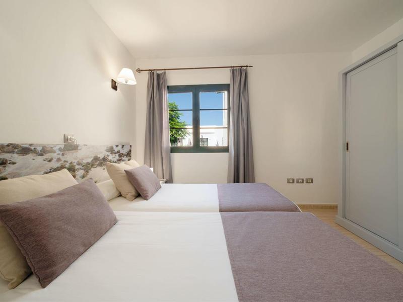 Schlichte Schlafzimmer mit zwei Einzelbetten, grauen Decken, Kissen und Fenster mit Vorhängen.