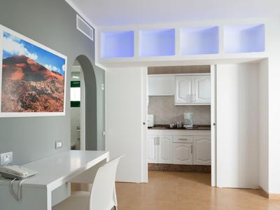 Bright room with desk, chair, open door to kitchen, and large artwork on the wall.