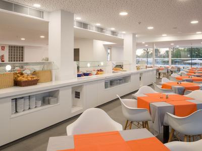 Modern breakfast room with orange-covered tables and white chairs, bright and open atmosphere.