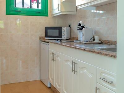 Angolo cucina luminoso con armadietti bianchi, microonde e piano di lavoro in marmo accanto a finestra verde.