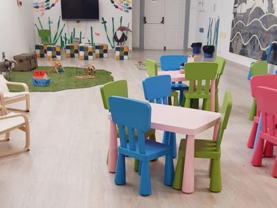 Sala giochi colorata per bambini con piccoli tavoli e sedie, arte murale e piante.