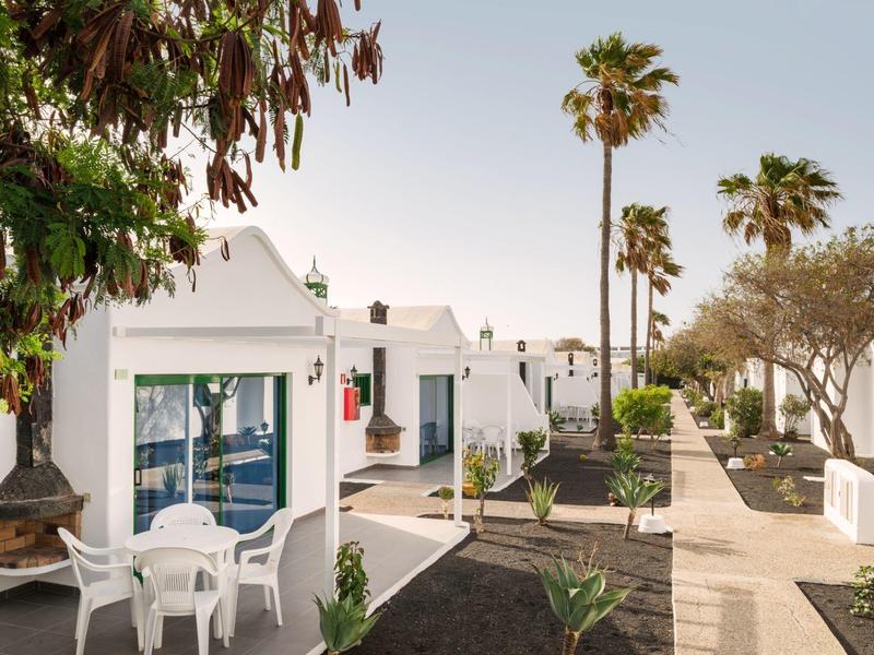 Bungalow bianchi con area esterna e palme in una giornata limpida.