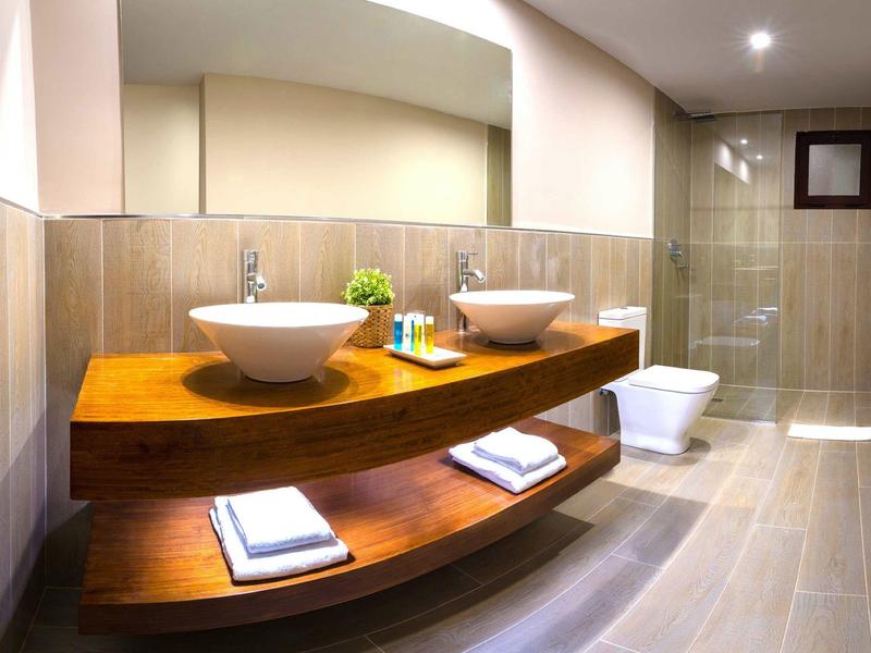 Modernes Badezimmer mit Holzregalen, zwei weißen Waschbecken und hellen Fliesen.