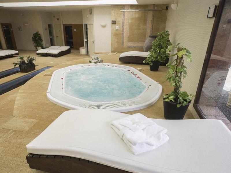 Moderner Wellnessraum mit rundem Whirlpool, Pflanzen und weißen Liegen mit Handtüchern.