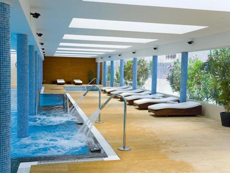 Moderner Indoor-Pool mit Whirlpool, Liegen, großen Fenstern und hellem, offenem Raum.