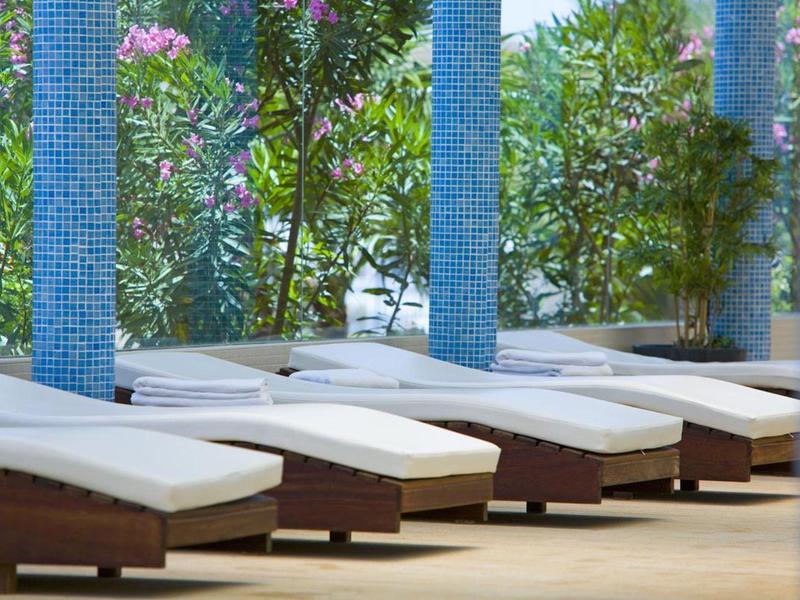 Mehrere weiße Liegen mit brauner Unterlage stehen nebeneinander auf einer Terrasse mit blauen Säulen.