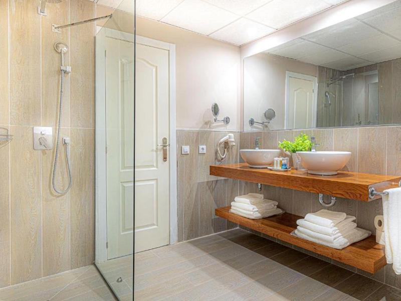 Helles Badezimmer mit Glasdusche, Holzwaschtisch, großen Spiegeln und weißen Handtüchern auf Regalen.