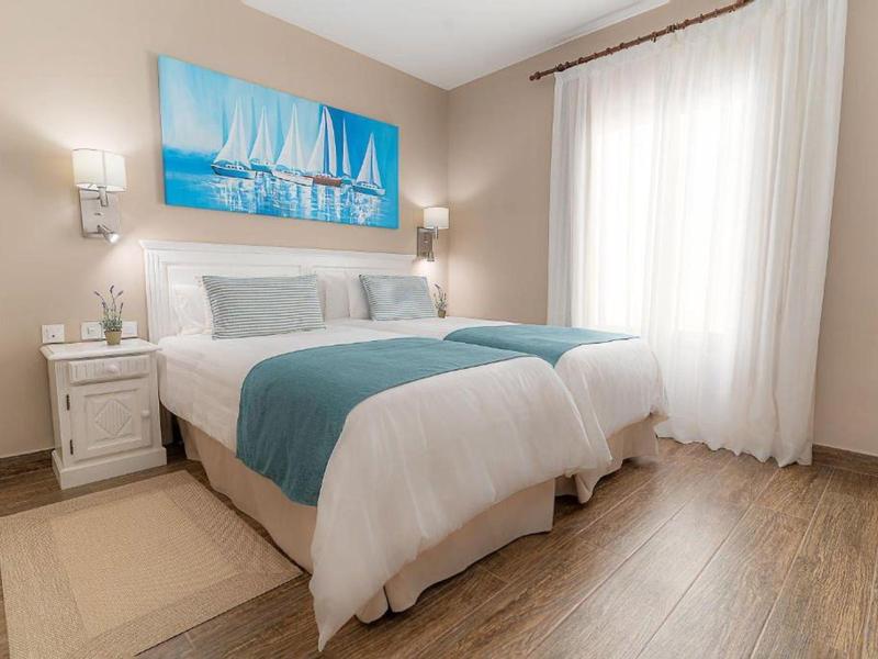 Schlichtes Schlafzimmer mit Doppelbett, weißen und blauen Bettdecken, Holzboden und blauem Segelbootbild.