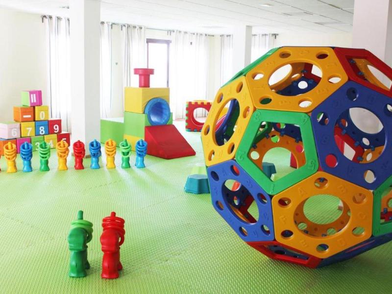 Bunter Spielraum mit großen Bauklötzen, Figuren und einem kugelförmigen Steckspiel auf grünem Boden.