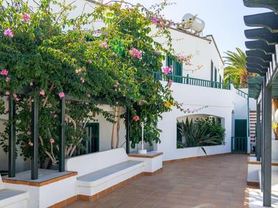 Cortile con panchine bianche e piante di bouganville in fiore con sole.