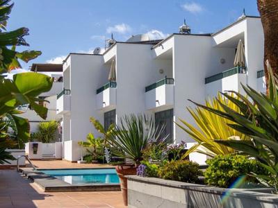 Weiße moderne Gebäude mit Balkonen neben einem schmalen Pool und üppigem tropischem Grün.