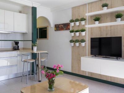 Soggiorno moderno con cucina bianca e TV a parete.