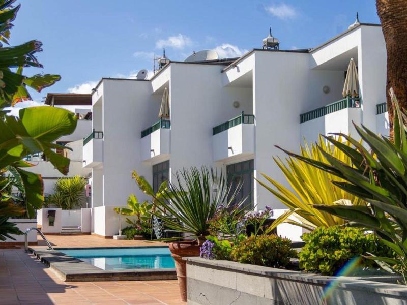 Edifici di hotel bianchi moderni con balconi, circondati da piante tropicali e piscina.