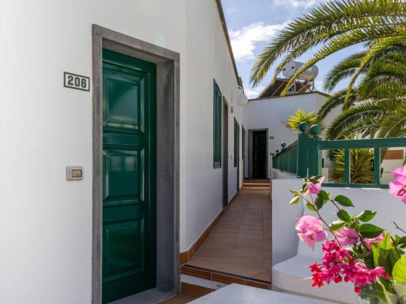 Accesso stretto al balcone con porta verde e pareti bianche, decorato con palme e fiori.