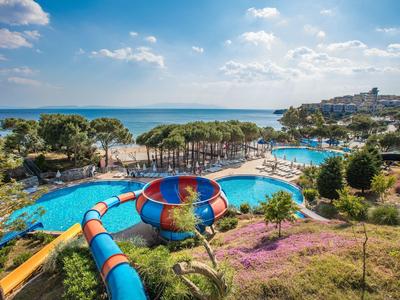 Groot buitenzwembad met glijbaan en uitzicht op zee onder blauwe lucht.