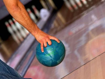 Eine Person hält eine blaue Bowlingkugel und zielt auf die Pins am Ende der Bahn.