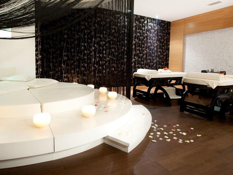 Moderne wellnessruimte met jacuzzi, kaarslicht en massagetafels in een ontspannen sfeer.