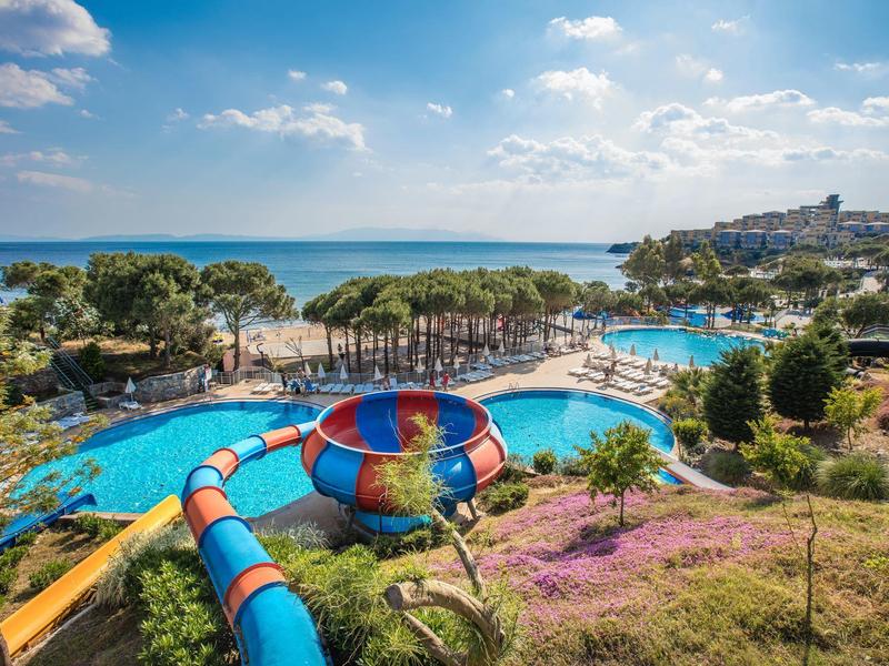 Groot buitenzwembad met glijbaan en uitzicht op zee onder blauwe lucht.