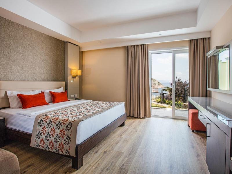 Lichte hotelkamer met groot bed, modern interieur en balkon met uitzicht op zee.