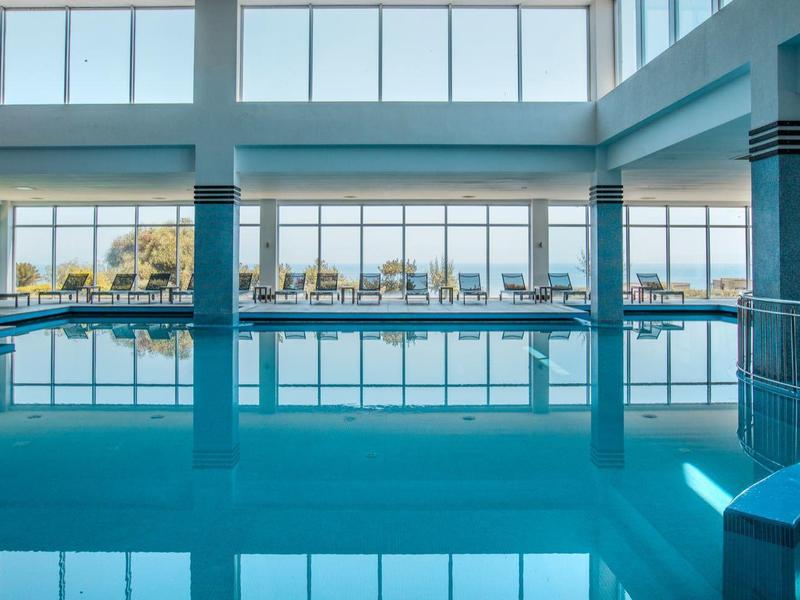 Overdekt zwembad met grote ramen en ligstoelen met uitzicht op zee.