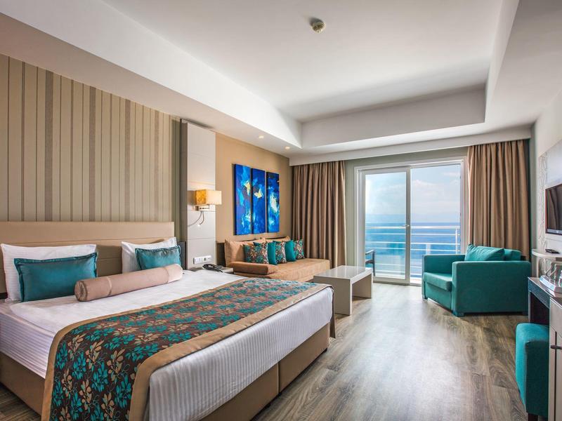 Moderne hotelkamer met groot bed, zithoek en zeezicht door grote ramen.