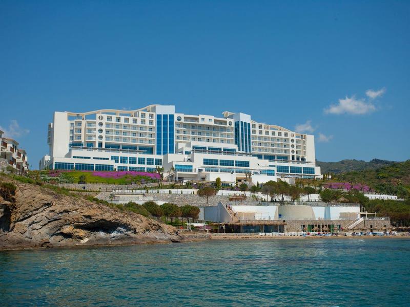 Modern hotel op een heuvel met uitzicht op zee onder een heldere blauwe lucht.