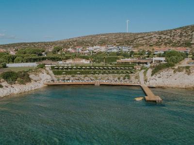 Kustresort met pier, helder water en zonovergoten heuvelachtige achtergrond.