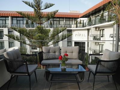 Gemütliche Terrasse mit Sitzgruppe, Tisch und Blumen vor einem mehrstöckigen Hotelgebäude.