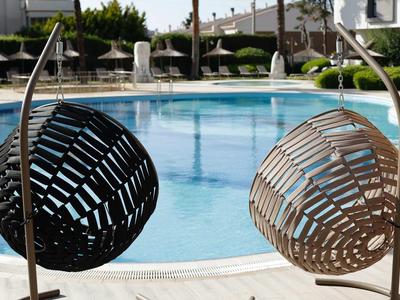 Twee hangstoelen naast een rond zwembad in een buitenruimte van een hotel.