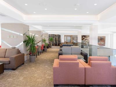 Moderne hotel-loungeruimte met sofa's, fauteuils en planten in een lichte omgeving.