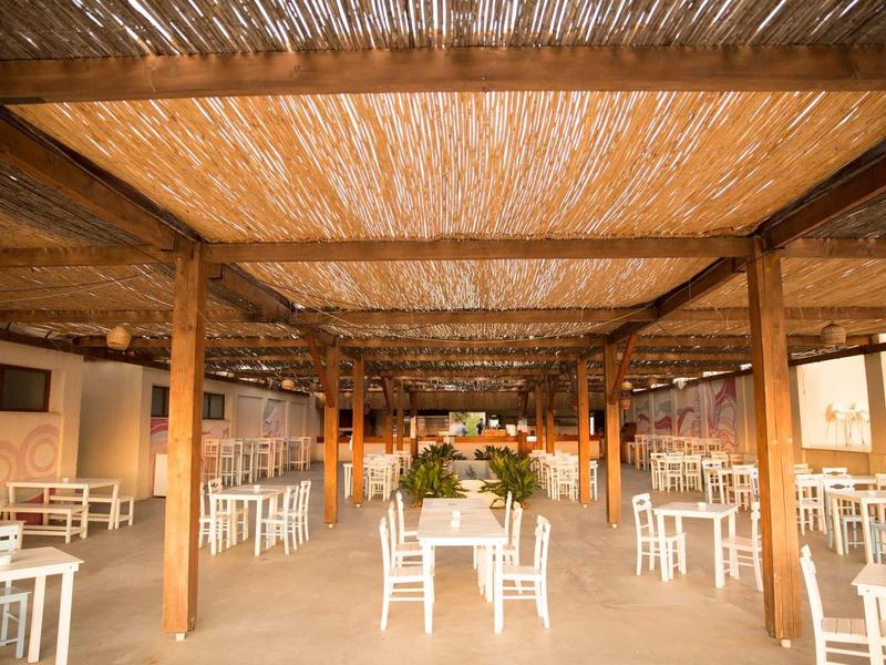 Grote open eetruimte met witte stoelen, houten balken en natuurlijk dak.