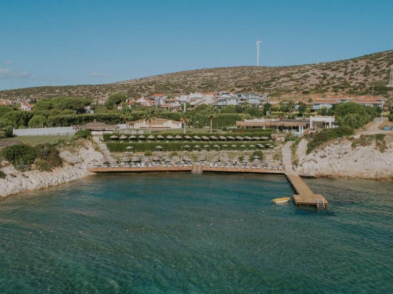 Kustresort met pier, helder water en zonovergoten heuvelachtige achtergrond.