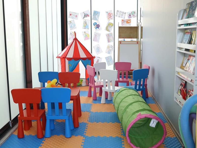 Kleurrijke speelruimte voor kinderen met kleine stoelen, tafel, tent en tunnel in een kamer.